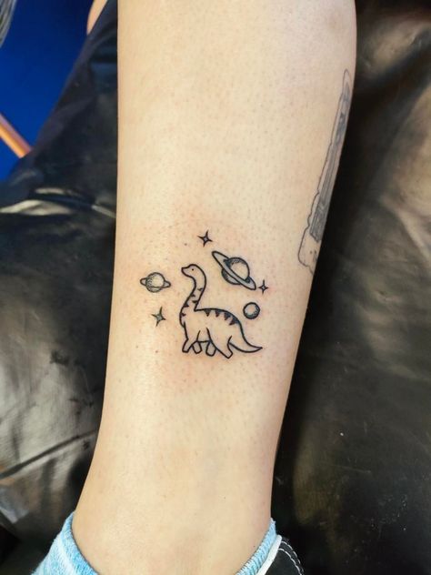 Small dinosaur tattoo in space. T Rex Space Tattoo, Cute Tattoos Dinosaur, Cute Dino Tattoo Matching, Dinasour Tattoo Matching, Small Tattoo Dinosaur, Star And Space Tattoos, Cute Matching Dinosaur Tattoo, Patchwork Dinosaur Tattoo, Cow On A Skateboard Tattoo