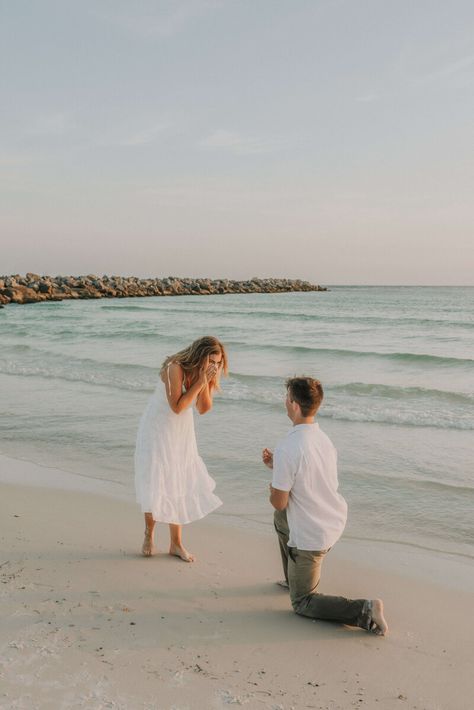 Young couple dressed in white & neutral summer clothing - on shore of beach in St Andrews State Park, PCB Florida.  Young man is kneeled down on one knee, with ring outstretched, girl is excitedly covering her face with her hands. Photo taken by intimate wedding & portrait photographer Brittney Stanley of Be Seen Photos Simple Proposal Ideas Beach, Surprise Beach Engagement, Surprise Proposal Photoshoot Beach, Marriage Proposal Beach, Engagement At The Beach, Proposal Beach Photos, Engagement Proposal Ideas Beach, Engagement Photos Surprise, Surprise Beach Proposal