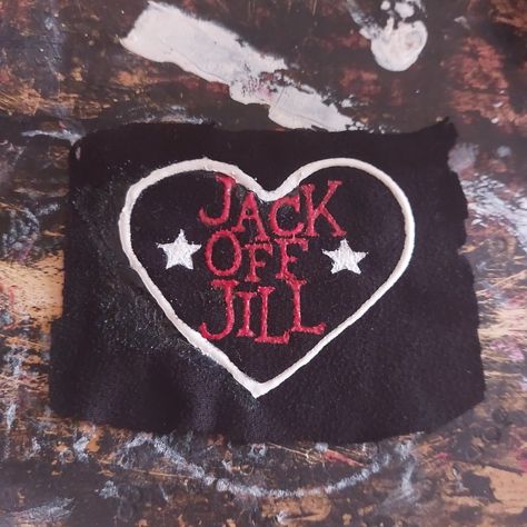 An unevenly cut, black, rectangle, fabric patch is on a paint-stained background. On the patch is a white heart, inside the heart, written in red, are the words "Jack Off Jill" in a vertical column. On either side of the word "Off" are white stars. Jack Off Jill Logo, Punk Shirts Diy, Punk Pins And Patches, Punk Band Patches, Band Patches Diy, Jack Off Jill Band, Patch Ideas Punk, Punk Diy Ideas, Crust Patches