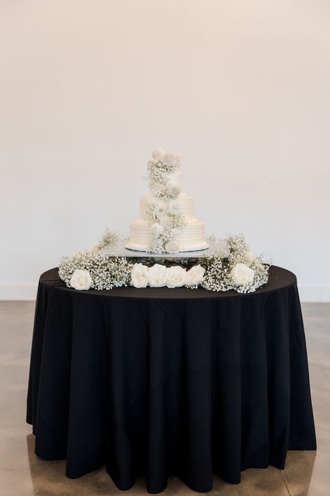 Three tiered white wedding cake on a black wedding dessert table. The neutral cakes was decorated with white roses and baby's breath cascading down to create an extra pop of personality for this elegant monochromatic wedding at the  Diamond Creek Farms in Nashville, TN | John Myers Photography & Videography White And Black Dessert Table, Black White Dessert Table, Black And White Wedding Dessert Table, Wedding Mexican Food, Neutral Cakes, Grooms Cake Tables, Wedding Cake Display Table, White Dessert Tables, Mexican Food Ideas