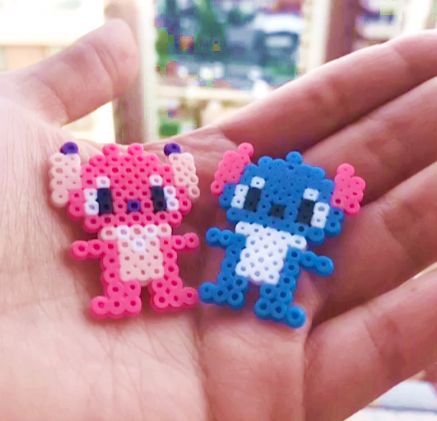 Uma mão cor de pele clara aberta, segurando dois bonecos, um da Angel(rosa e rosa claro) e um do Stitch(azul e branco) do filme Lilo & Stitch, feito de hama beads ou perler beads, que são como bolinhas, para fazer artesanato, formas, personagens, etc. Perler Beads Stitch, Hama Disney, Mini Hama Beads, Beads Stitch, Melty Bead Designs, Ironing Beads, Melt Beads Patterns, Angel Stitch, Easy Perler Beads