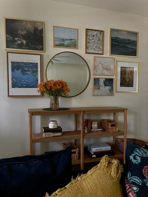 Entryway gallery wall including impressionist art prints and a gold mirror. A light wood console bookcase and lightly styled shelves with a few classic books, fashion books, and candles. Gallery Wall Console Table, Gallery Wall Round Mirror, Round Mirror With Pictures Around It, Console Table Gallery Wall, Gallery Wall With Circle Mirror, Wall With Console Table, Gallery Wall With Round Mirror, Gallery Wall Above Console Table, Mirror And Picture Wall Layout