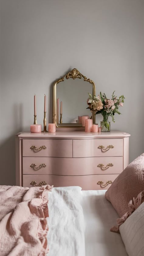 A soft blush pink dresser with gold handles, set against a light gray wall, adorned with delicate decor items like a gold-framed mirror, candles, and fresh flowers. Baby Pink Dresser, Vintage Pink And Gold Bedroom, Pretty Minimalist Bedroom, Pink And Gold Dressing Room, Pink Academia Room, Pink And Gold Bedroom Aesthetic, Cute Dresser Decor Aesthetic, Pink Vintage Aesthetic Room, Pink And Gold Closet