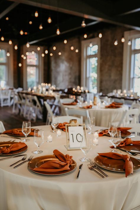 Fall Wedding Reception Table Decor with Rust Silk Napkins and White Linens | Edison Bulb Lighting Fall Wedding Napkins Place Settings, Fall Wedding Table Linens, Fall Color Wedding Table Decor, Fall Wedding Table Linen Ideas, Round Table Wedding Decor Burnt Orange, Chic Fall Wedding Decor, Subtle Fall Wedding Decor, Rust Wedding Ceremony Decor, Rust Orange Table Setting