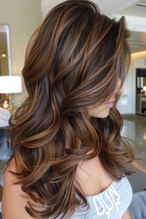 Woman with long, wavy brown hair with highlights styled in loose curls.