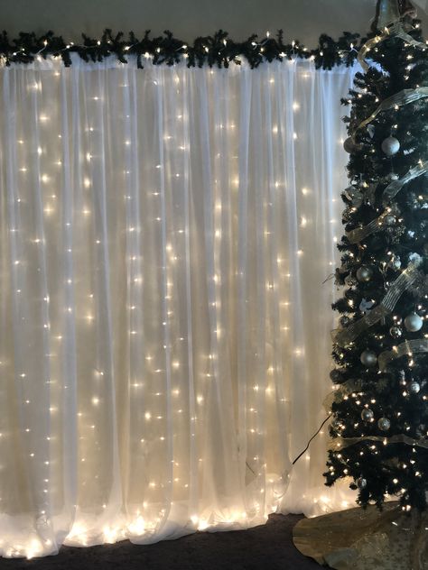 Christmas Backdrop (Pipe and Drape with string lights and greenery. Christmas Party Room Decorations, Christmas Photo Corner Ideas, Christmas Drapes Ideas, Winter Theme Backdrop, Winter Party Backdrop, Christmas Pictures Backdrop, Simple Christmas Backdrops For Photos, Diy Backdrop Christmas, Christmas Wedding Photo Backdrop