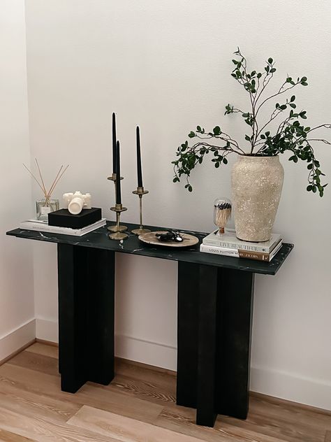 Entryway Console table decor Console Table : Burke Decor Vase : Pottery Barn Plant stems: Amazon Camera Candle : Gift from @kelir from CB2 Diffuser: Pottery Barn Black Candles: Amazon Candle Stand : Gift from @anniemescall Coffee Table Books : Amazon #homedecor #home #entrywaydecor #consoletable #homestyle Hallway Stand Entry Tables, Vase On Entryway Table, Walkway Table Decor, Small Black Entryway Table, Entrance Table Decor Modern, Black Console Table Styling, Black Coffee Table Styling, Black Entry Table Decor, Black Console Table Entryway