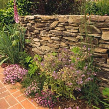 A dry-stacked stone wall looks so natural. The spaces between stones in the retaining wall allow water to drain through, relieving pressure. Another advantage of dry-stacked stone walls is that you can create planting pockets for small rock garden plants such as sedums. Garden Landscaping Design Ideas, Stone Walls Garden, Stacked Stone Walls, Dry Stack Stone, Gravel Landscaping, Backyard Garden Layout, Rock Garden Plants, Rock Garden Design, Dry Stone Wall