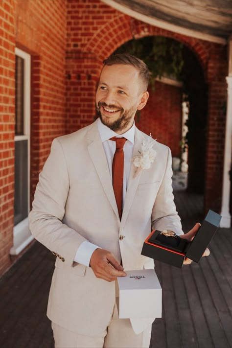 A groom smiling to someone off camera holding a gifted watch. Cocktail Attire Men Wedding, Cream Wedding Suit, Cream Suits For Men, Garden Party Outfits, Burnt Orange Tie, Cocktail Attire Men, Beige Suit, Groom And Groomsmen Suits, Cream Suit