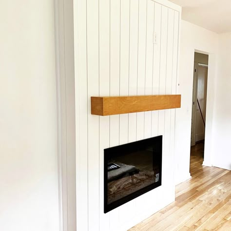 Fireplace surround in Lincoln, NE, featuring vertical shiplap painted white, black electric fireplace, and custom wood mantle in honey-colored stain. Shiplap On Sides Of Fireplace, Vertical Panel Fireplace, Shiplap Fireplace Vertical, Vertical Shiplap On Fireplace, Vertical Shiplap Mantle, Shiplap Vertical Fireplace, White Wood Panel Fireplace Wall, Vertical Paneling Fireplace, Diy Vertical Shiplap Fireplace