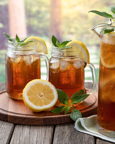 Pitcher of cold iced tea with mint, lemon slices and ice with two glasses ot tea on a wooden table and rural summer background Iced Tea Aesthetic, Summer Iced Tea, Unsweetened Iced Tea, Iced Tea Maker, Iced Tea Pitcher, Best Bagels, Tea Aesthetic, Salmon Potato, Waffle Cookies