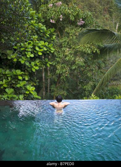 Woman bathing in an infinity pool surrounded by a lush tropical forest. Stock Photo Infinity Pool Tropical, Pool In Forest, Luxury Poolside, Tropical Colonial, Rent House, Indoor Waterfall, Infinity Edge Pool, Pool Waterfall, Outdoor Pools