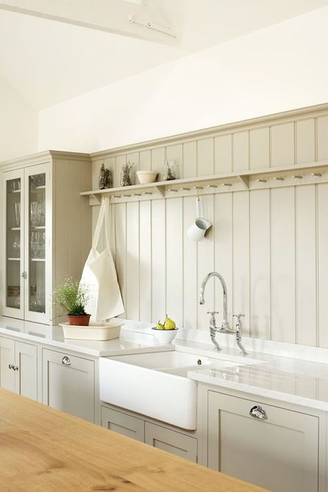 Stunning grey colored kitchen with custom shaker cabinets adorned with cup pull hardware alongside a dual farmhouse sink with bridge faucet framed by white stone counters which pair with a gray tongue and groove backsplash accented with cup hook shelf beside a countertop glass front hutch. Beadboard Kitchen Backsplash, Kitchen Devol, Beadboard Kitchen, Devol Kitchens, Beadboard Backsplash, Boot Room, Shaker Kitchen, Chic Kitchen, Cottage Kitchen