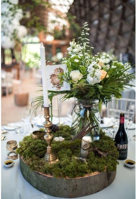 a woodland wedding centerpiece of a wood slice, moss, blooms and greenery in a jar, feathers and candles Woodland Theme Centerpieces Decor, Woodland Fairy Wedding Table Decor, Moss Decorations Wedding, Woodland Sweetheart Table, Woodland Theme Wedding Decorations, Enchanted Woodland Wedding, Enchanted Forest Wedding Table, Moss Table Decor, Moss Tablescape