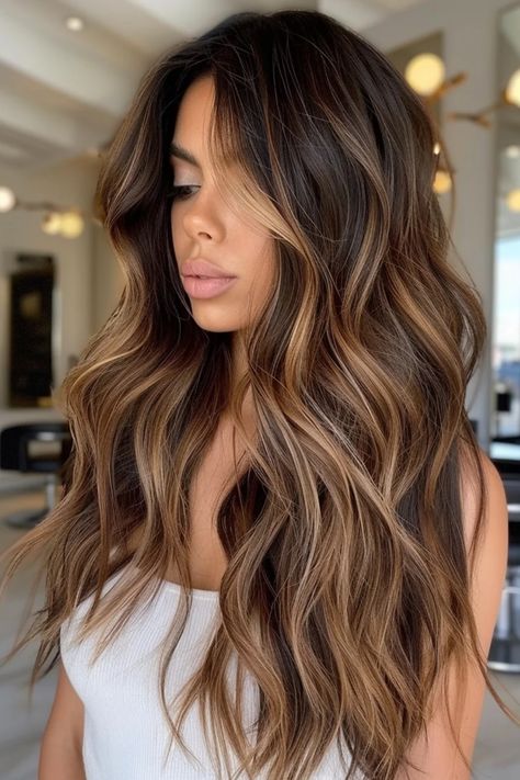 Woman with long, wavy, highlighted brown hair wearing a white tank top in a modern salon setting. Dark Root Caramel Balayage, Brunette With Brunette Highlights, Balayage Hair Blonde And Brown, Golden Balayage On Black Hair, Teasylights Dark Hair, Medium Brown Hair Balayage Caramel, Balayage For Wavy Hair, Hair Color With Dark Eyebrows, Transition From Dark To Light Hair