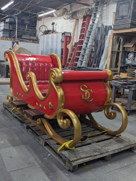 An ornate red sled with gold accents sits on a palette in the shop. Gold letters "SC" are embellished on the front of the sleigh to indicate that it's Santa's. Outdoor Sleigh Decor, Santa’s Sleigh, Santa Sleigh Decoration, Cranberry Farm, Novogodišnji Ukrasi, Christmas Fairytale, Santa Village, Christmas Santa Sleigh, Sled Decor