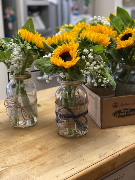 Sunflower centerpieces for our daughter’s graduation party. Mason jars from Walmart, sunflowers and baby’s breath from local grocery store, and ribbons and twine from Michael’s. I used double-side tape to attach the wide ribbon to the jars then tied the smaller ribbon around that. Add about 2-3 inches of water and you’re done. Sunflower Mason Jar Centerpieces, June Wedding Colors, Fairy Lights Wedding, Sunflower Centerpieces, Sunflower Vase, Party Table Centerpieces, Fall Activity, Western Parties, Mason Jar Ideas