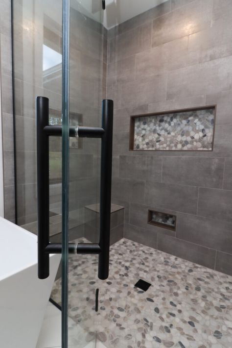 Gray tile shower with light pebble flooring. Glass shower door with black accents. Shower Tile Remodel Ideas, Gray Tiled Bathrooms Ideas, Gray Tile Master Bath, Grey Tile Shower Ideas Master Bath, Bathroom Shower Tiles Gray, Large Gray Tile Shower Ideas, Master Bath Grey Floor, Master Shower Dark Tile, Modern Restroom Ideas Shower Tiles