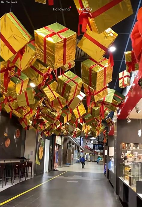 Hanging Christmas Presents From Ceiling, Presents Hanging From Ceiling, Warehouse Christmas Decor, Santa's Toy Factory Decorations, Christmas Ceiling Installation, Hanging Presents From Ceiling, Christmas Decor Restaurant Ideas, Christmas Decor Hotel, Ceiling Decor Christmas