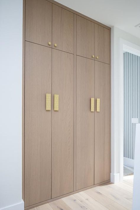 Brass hexagon hardware complements stacked floor-to-ceiling brown oak hallway cabinets. Hallway Storage Ideas, Oak Hallway, Hallway Cabinets, White Beveled Subway Tile, Hallway Storage Cabinet, Floor To Ceiling Cabinets, Beveled Subway Tile, Hall Cabinet, Hallway Cabinet