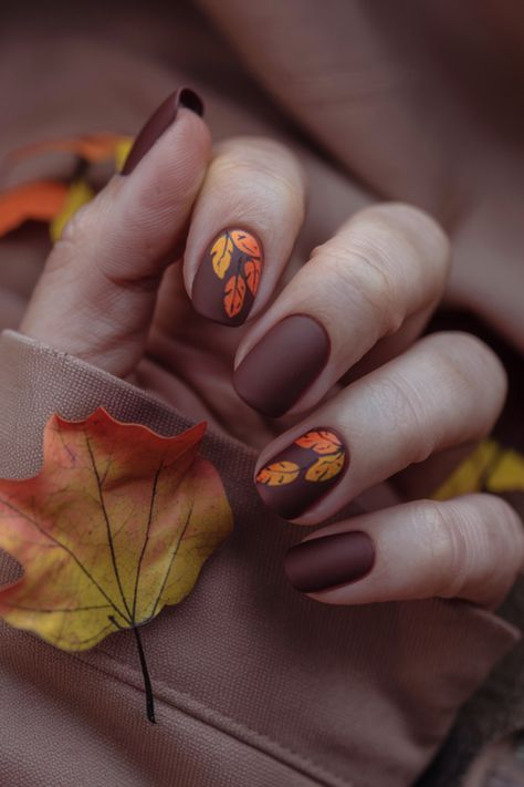 Capture the essence of fall with these chic brown nails, adorned with vibrant orange and yellow leaf designs. Perfect for the fashion-forward, this trendy fall nail design adds a seasonal touch to your look. Whether you're cozying up for the season or attending an autumn event, these stylish nails are the perfect accessory to elevate your fall fashion game! Fall Leaf Design Nails, November Themed Nails, Oval Nails Halloween, Leaf Nails Fall, Brown And Orange Nails Fall, Trendy Autumn Nails, Autumn Leaf Nails, Fall Leaf Nail Designs, Fall Leaves Nails