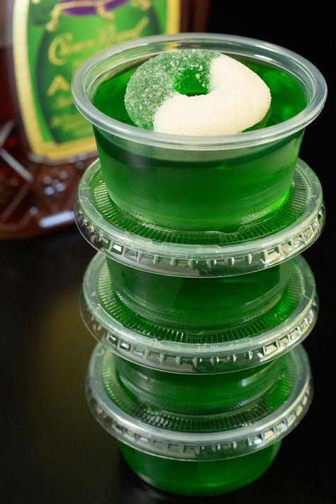 Four 2oz portion containers filled with Crown Apple jello shots are stacked on top of one another in front of a bottle of Crown Apple. Green Apple Fireball Jello Shots, Fairy Jello Shots, Apple Whiskey Jello Shots, Green Halloween Jello Shots, Crown Royal Apple Jello Shots, Apple Crown Jello Shots, Green Tea Jello Shots Recipe, Crown Apple Jello Shots, Crown Royal Jello Shots