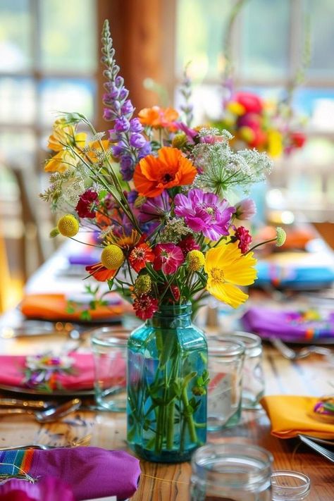 Create a magical atmosphere with wildflower centerpieces at your wedding. These simple and beautiful flower arrangements, perfect for round and rectangle tables, use mason jars or vases, offering DIY charm for showers and birthdays.Clear chat Vase With Wildflowers, Wildflower Table Arrangements, Colorful Flowers Wedding Table, Simple Summer Wedding Table Decor, Spring Centerpiece Ideas Wedding, Wedding Round Table Decor, Wildflower Wedding Centerpiece, Summer Wedding Flower Arrangements, Wildflower Wedding Decor