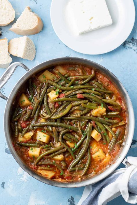 Top-down view of cooked fasolakia yiahni in a stainless steel sauté pan with bread and feta cheese in the background. Fasolakia Yiahni, Greek Green Beans, Sauteed Tomatoes, Beans And Potatoes, Braised Greens, Potatoes Tomatoes, Greek Dinners, Green Beans And Potatoes, Healthy Vegetable Recipes