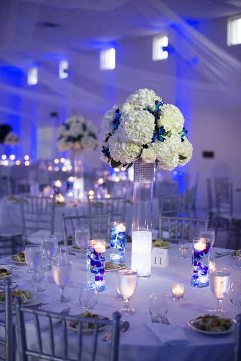 White and Silver Reception Decor with Blue Uplighting Wedding Decorations Blue, Royal Blue Centerpieces, Silver Wedding Centerpieces, Blue Uplighting, Royal Blue Wedding Theme, Blue Wedding Receptions, Royal Blue Quince, Uplighting Wedding, Quinceanera Centerpieces