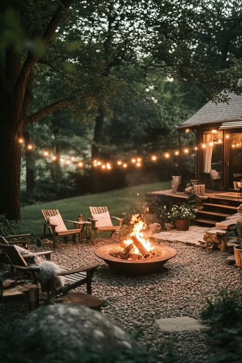 Cozy outdoor fire pit area with string lights, surrounded by wooden chairs and lush greenery. Fire Outside Ideas, Fire Pit With Rocks Natural Stones, Modern Backyard Fire Pit Ideas, Outdoor Living Lighting Ideas, Garden Design With Fire Pit, Backyard Gathering Space, She Shed With Fire Pit, Bonfire Pits Backyard, Cozy Backyard Fire Pit Ideas