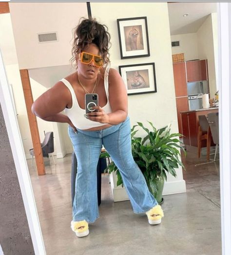 Lizzo taking a selfie wearing a white tank top, light wash wide leg jeans with a center seam, fuzzy yellow platform sandals, oversized orange aviators, and a messy top knot Lizzo Outfits Casual, Lizzo Aesthetics, Annika Osterlund, Lizzo Outfit, Lizzo Outfits, Lizzo Concert, Celebrity Face Claims, She A Baddie She Know, Fame Shifting