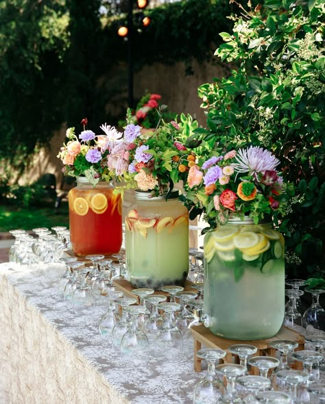 three beverage dispensers are decorated with flowers and spa water Self Serve Drinks Wedding, Wildflower Cocktail Hour, Garden Party Cocktail Tables, Wedding Juice Bar Ideas, Garden Party Wedding Cocktail Hour, Garden Party Aesthetic Wedding, Whimsical Garden Wedding Reception, Round Wedding Bar, Wedding Bar Inspiration