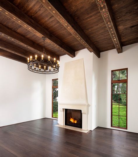 Spanish Mediterranean Elegance Plaster fireplace, custom iron chandelier, hand painted wood beams, wood floor | Santa Barbara Mediterranean Mediterranean Fireplace, Spanish Mediterranean Homes, Colonial Revival House, Painted Beams, Santa Barbara Style, Spanish Mediterranean, Dark Wood Cabinets, Iron Chandeliers, Mediterranean Home