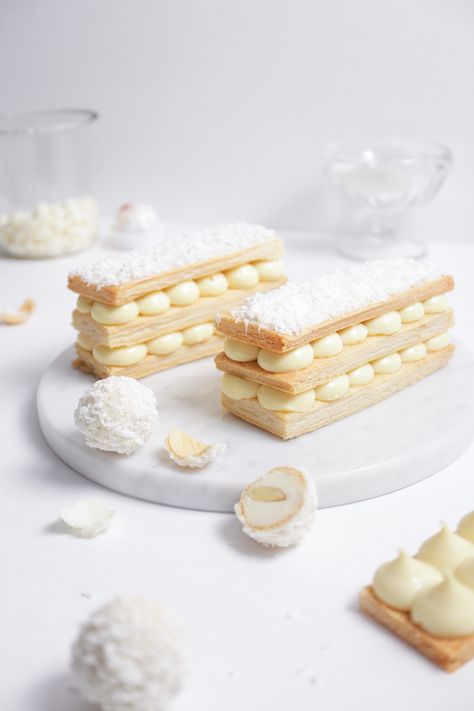 two stacks of mille-feuille filled with small dollops of white chocolate coconut pastry cream, raffaellos around, cup with white chocolate in background White Chocolate Pastry, White Chocolate Pastry Cream, Coconut Pastry Cream, Mille Feuille Recipe, Mille Feuille Wedding Cake, Mille Feuille Plating, Mille Feuille Cake, Plated Mille Feuille, Coconut Tart