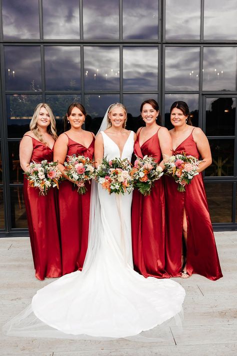 Bridesmaids in matching red satin bridesmaid dresses with leg slit posing with the bride with her curled blonde hair in sleek hairstyle with fitted wedding dress Champagne Bridesmaid Dresses Red Flowers, Light Red Bridesmaid Dresses, Red Bridesmaid Dresses Summer, Bridesmaid Red Dresses, Red Satin Bridesmaid Dresses, Red Bridesmaids Dresses, Doughnut Tower, Bridesmaid Dresses Red, Bridesmaid Dresses Red Long