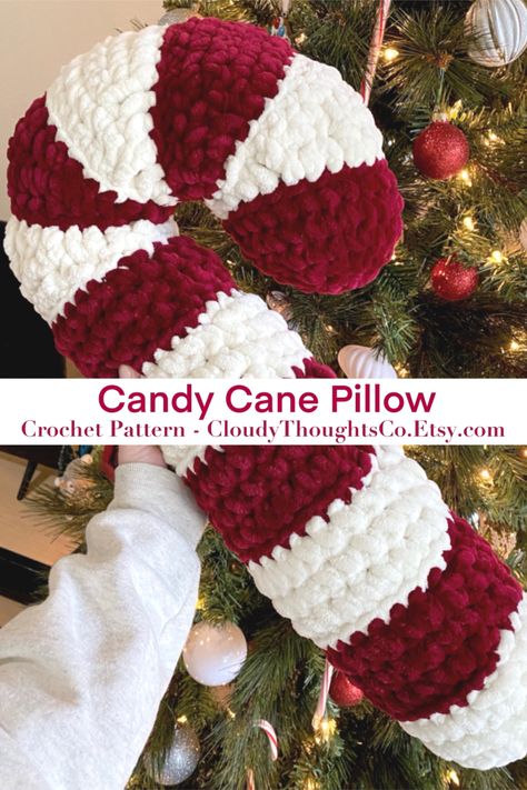 A hand holding an oversized crochet candy cane pillow in front of a Christmas tree. The  pillow is fluffy with burgundy and cream stripes. Crochet Candy Cane, Candy Cane Pillow, Crochet Candy, Crafts Cute, Crochet Decor, Winter Crochet, Crochet Xmas, Crochet Bedspread, Crochet Design Pattern