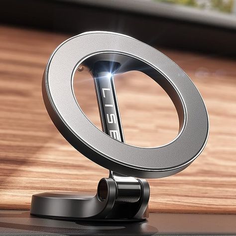 The photo shows a silver, steel alloy circular phone mount that uses MagSafe technology to hold the device in place.  It shows the mount set up on a flat surface with a wood panel behind it. Iphone Car Holder, Car Cell Phone Holder, Mobile Phone Stands, Magnetic Phone Holder, Latest Iphone, Support Telephone, Car Holder, Cell Phone Holder, Phone Mount