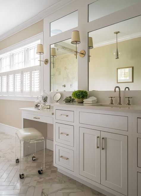 A rolling acrylic vanity stool sits on marble chevron floor tiles at a white drop down vanity finished with nickel pulls and an off-white quartz countertop. Bathroom Vanity Sit Doen, White Bathroom Vanity Chair, Simple Master Bath With Vanity Seat, Single Sink With Makeup Vanity, Sit Down Vanity, White Vanity With Glass Top, White Marble Bathroom Floor Wood Vanity, Stool With Wheels, Acrylic Vanity