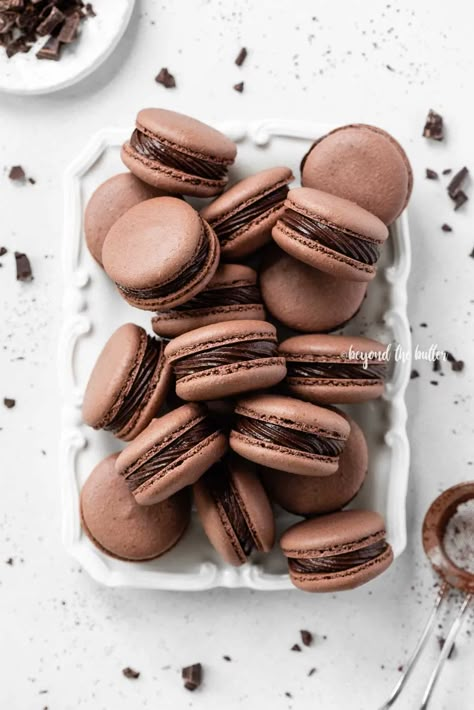 These Dark Chocolate Macarons have a light crisp, outer layer with a chewy, chocolatey center that are filled with a rich, dark chocolate fudge frosting. They're bite-size, decadent treats that are easier to make than you might think! Recipe on BeyondtheButter.com, includes helpful tips and tricks. #chocolatemacarons #macarons #swissmethod #frenchmacarons Kue Macaroon, Chocolate Macarons, Macaron Filling, Chocolate Macaroons, Macaron Recipes, Dark Chocolate Fudge, Chocolate Fudge Frosting, Chocolate Macaron, Fudge Frosting