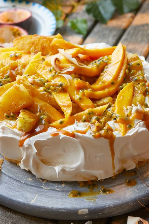 A pavlova base topped with mango slices, passion fruit seeds, roasted pineapple pieces and toffee sauce Pavlova Mango Passion Fruit, Tropical Fruit Pavlova, Mango Pavlova Recipe, Mango Pineapple Dessert, Pavlova Food Photography, Pavlova Tropical, Tropical Pavlova, Carribean Desserts, Mango Pavlova