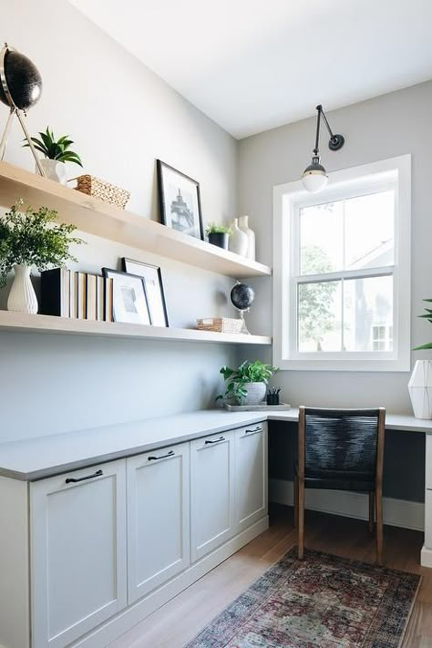 Blond wooden shelves are styled and stacked over a built-in l-shaped desk boasting white shaker cabinets and a gray desk top seating a black rope chair. Coastal Home Office, Best Benjamin Moore Paint Colors, Coastal Office, Working Room, Benjamin Moore Paint Colors, Modern Coastal Home, House Move, Home Bunch, Modern Farmhouse Home