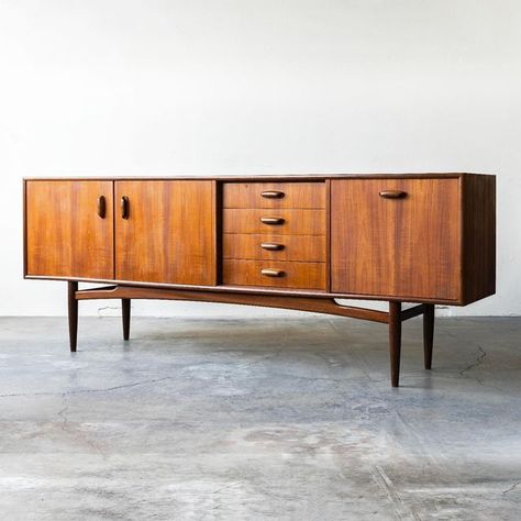 Mid-Century Modern Furniture on Instagram: "G-Plan Fresco, teak, British sideboard designed by V.B. Wilkins.⁠ ⁠ Features:⁠ ⁠ • Beautiful teak woodgrain through-out⁠ • Drop-down bar⁠ • Center drawers⁠ • Doors open to an open fixed shelf⁠ • Model 4058⁠ • Body stands on a frame of turned legs joined by an arched crossbar⁠ • Sculpted teak hardware⁠ • Ample storage⁠ ⁠ Dimensions:⁠ 81“W x 31”H x 18“D⁠ ⁠ Visit the website to learn more and/or to get a shipping quote.⁠ ⁠" Mid Century Sideboard, Teak Sideboard, Sideboard Designs, Turned Leg, Mid Century Modern Furniture, Door Opener, Wood Grain, Sideboard, Modern Furniture