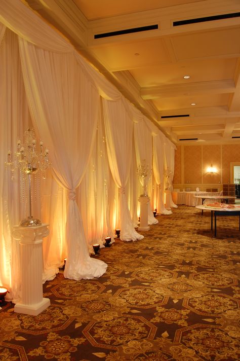 White Backdrop with Amber LED Up Lighting #whitechiffon #fabricbackdrop #amberuplighting #uplighting #AmberLED #weddingbackdrop #weddingdecor #michiganweddings #colonialevents Backdrop Lighting Ideas, Wedding Wall Drapes, Met Gala Design, Quince List, Gold Shimmer Background, Yellow Quince, Event Space Decor, Outdoor Christmas Party, Wall Drapes