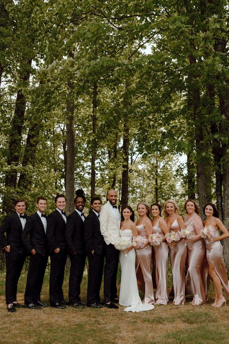 Wedding party in black groomsmen suits and pink satin bridesmaid dresses. Black Tux And Champagne Wedding, 6 Bridesmaids And Groomsmen, Blush Pink Bridesmaid Dresses With Groomsmen, Blush Pink Bridesmaids And Groomsmen, Champagne Pink Bridal Party, Tan And Pink Wedding Colors, Wedding Ceremony Bridesmaids Groomsmen, Groommaids Suit, Bridesmaid Dresses Champagne Pink