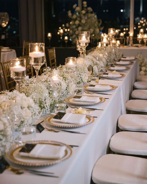 Transform your reception into a regal affair with intricate gold tablescape details. White florals, statement candles and the gold accents create an ambiance of opulent elegance. ✨   #weddingtablescape #tabelscapedesign #weddingreception #weddinginspo #weddingdetails #weddingdecor #weddingstyle #weddingplanner #nycweddings #overthemoon #stylemepretty #luxuryweddings #caratsandcake #alinatoevents Reception Table Decorations Candles, Elegant Outdoor Wedding Reception Table Arrangements, Timeless Wedding Tablescape, Long Dining Table Wedding, Neutral Wedding Decorations Receptions, White Wedding Design, Classic Elegant Wedding Table Setting, White Floral Wedding Table Decor, White And Gold Wedding Aesthetic