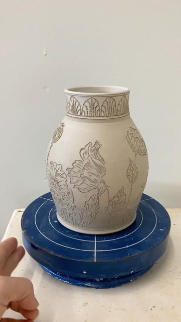 Ayla Mullen on Instagram: "I finished carving this Poppy vase today! 🌸 Tomorrow I will scrub off all the little clay bits at the edges of the carvings and inlay blue underglaze into the design. I haven't worked much with poppy designs in the past few months, and it felt good to come back to my favorite flowers. I really can't say why they're my favorite-- something about the expressiveness of every stage of bud, bloom, and seed pod captivates me endlessly. What is your favorite flower? #pop Poppies On Pottery, Pottery Vase Ideas Design, Ceramic Flower Carving, Ceramics Carved Designs, Carved Vases Pottery, Carved Flowers Pottery, Feminine Pottery, Ceramic Vase Design Ideas, Carved Vases Ceramic Pottery