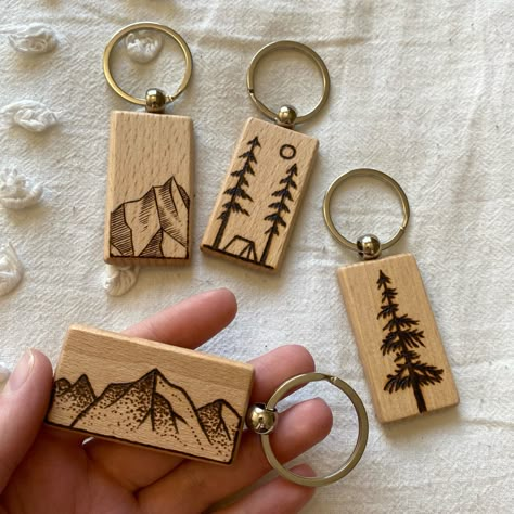 There are 4 wood rectangular keychains with woodburned designs. There is a vertical mountain, horizontal mountain, a cedar tree and a camping themed one. Wood Burned Magnets, Keychain Wood Ideas, Woodburning Keychain Ideas, Woodburned Keychain Ideas, Painted Wooden Keychain Ideas, Wood Burned Keychain Ideas, Wood Burn Keychain, Wood Burning Keychains, Wood Burning Keychain