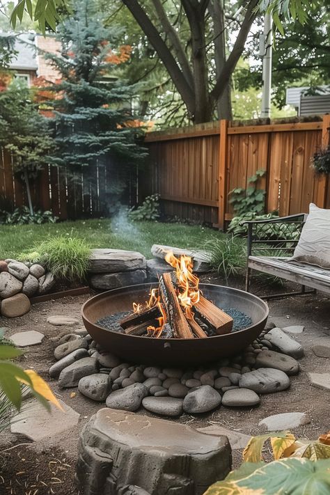 A cozy backyard with a fire pit surrounded by rocks, a wooden fence, and lush green trees and plants, perfect for relaxing outdoors. Outside Rock Fire Pit Ideas, Diy Fire Pit Sitting Area, Pea Gravel Fire Pit Area Diy, Fire Pit With Half Wall, Fire Pit Circle Ideas, Circle Fire Pit Area Diy, Cool Backyard Features, Creekside Fire Pit, How To Level Ground For Fire Pit Area