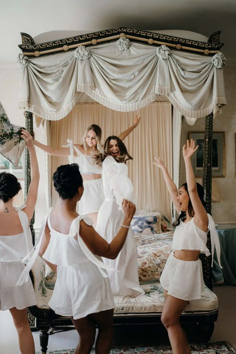 A bride wearing a long white robe parties with her bridesmaids in the honeymoon suite on her wedding morning as they get ready. The scene embodies joy and excitement with all the ladies smiling gleefully. Bridesmaids Helping Bride Get Dressed, Italian Wedding Getting Ready, Wedding Get Ready Aesthetic, Getting Ready Day Of Wedding, Bridesmaid Morning Of Wedding, Wedding Getting Ready Ideas, The Morning Of The Wedding, Bridesmaids Morning Of Wedding, Bridal Party Morning Of Wedding