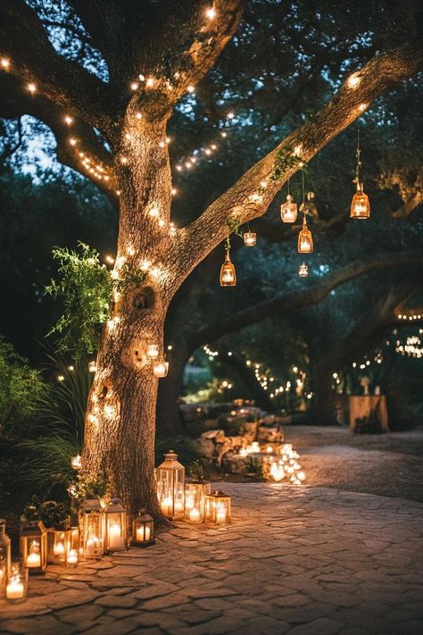 Enchanted forest theme wedding outdoor decor with a tree decorated with fairy lights and tiny lanterns under the tree there is a paved ground lined. Let your big day become a magical woodland affair with these enchanting forest wedding ideas that’ll make your guests feel like they’ve stepped into a fairy tale. Wedding Fairy Aesthetic, Jewel Tone Enchanted Forest Wedding, Tree Lanterns Wedding, Enchanted Forest Wedding Arbor, Forest Wedding Photo Booth, Cabin Wedding Decorating Ideas, Secret Garden Themed Prom, Enchanted Forest Venue Decor, Practical Magic Themed Wedding